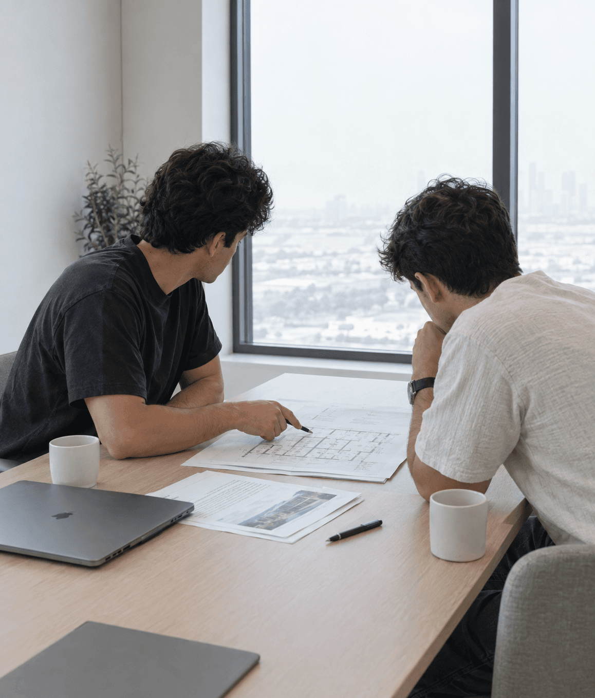 A property consultant talking a client through a floor plan at a table in a bright meeting room.