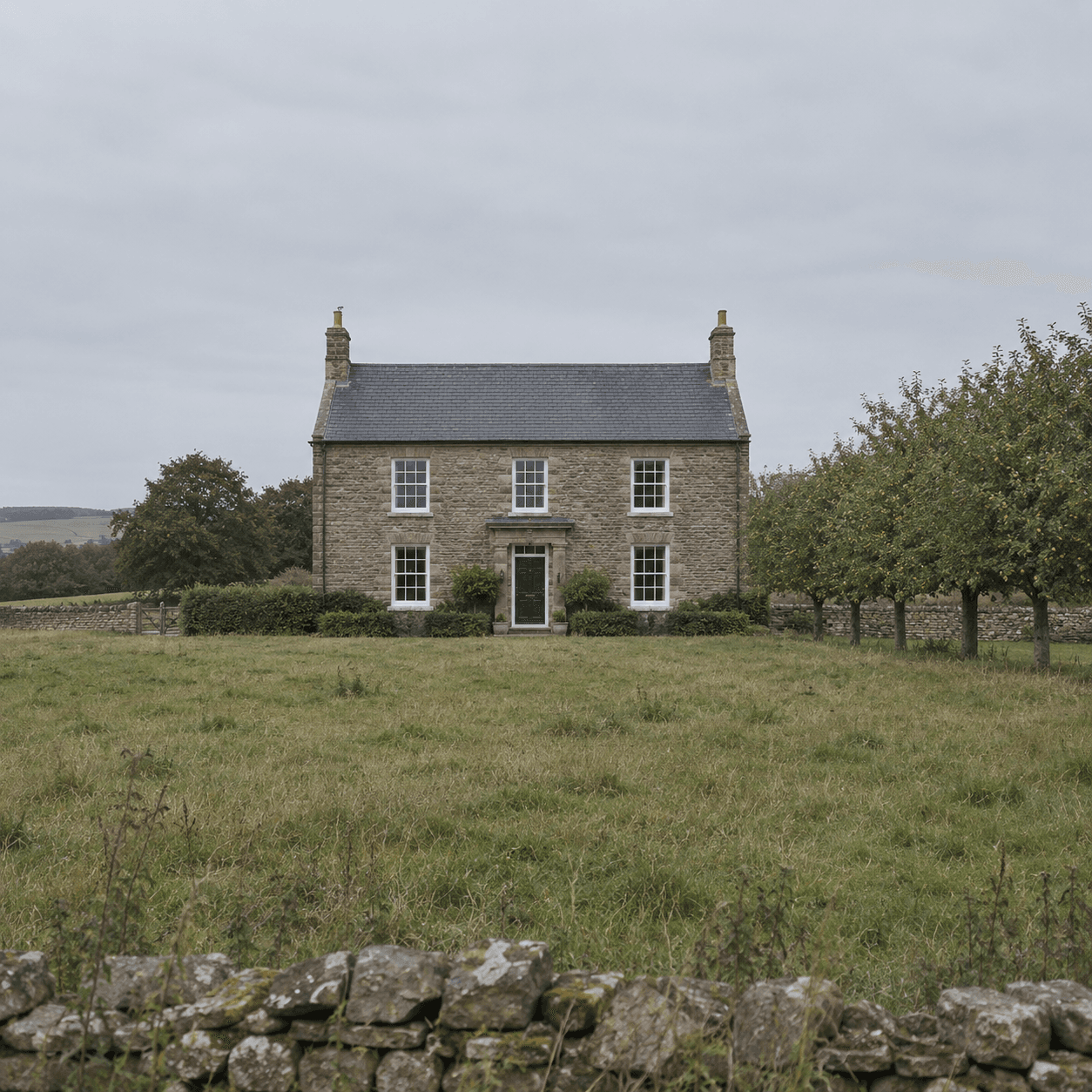 Stone country house seen across a grass field with rows of fruit trees.