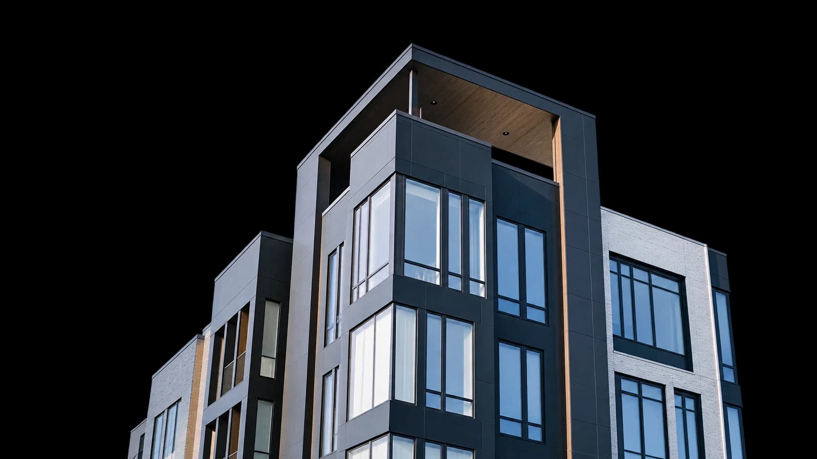 A modern mid-rise apartment building with dark charcoal panels, pale brick and timber soffits, seen from below.